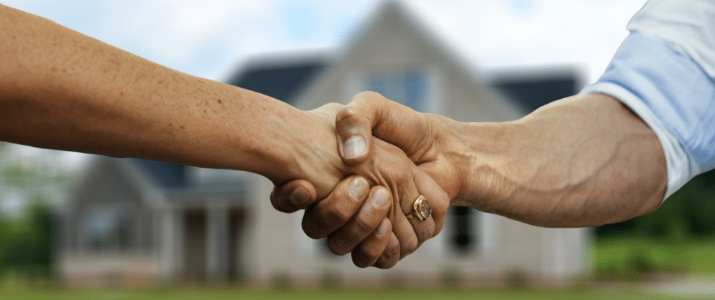 Close-up handshake between two people in front of a house, symbolizing a successful and stress-free home sale.
