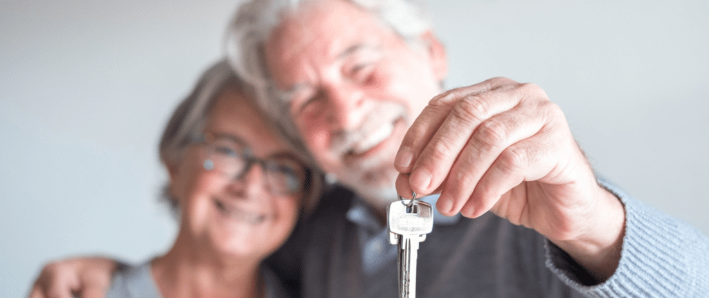 Smiling senior couple holding out house keys, representing the ease and satisfaction of selling a home to a cash buyer.